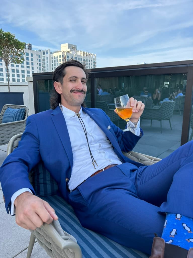 Phen at a rooftop bar with a beer, a sick mullet, and a sweet mustache